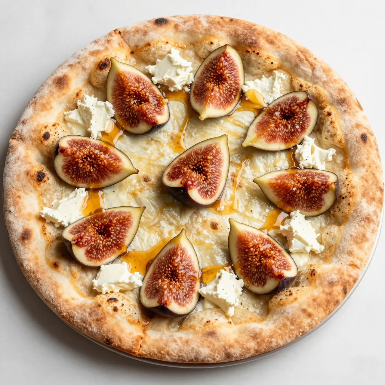 Top view of a freshly baked flatbread pizza topped with figs, goat cheese, and honey drizzle on a light countertop.