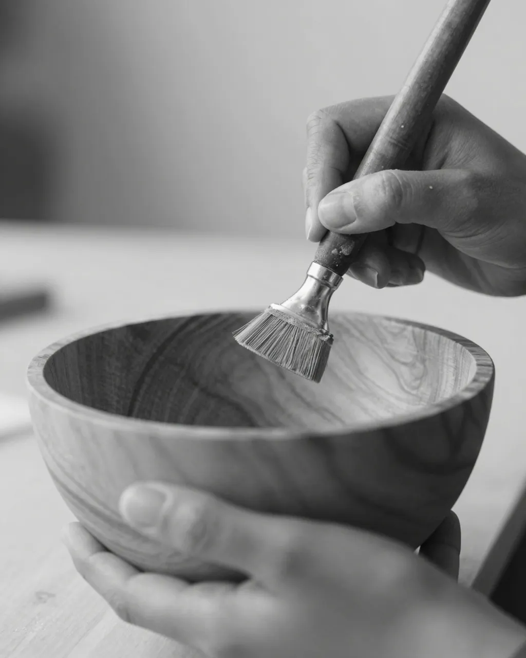 Black and white close-up of a person's hands brushing a turned wooden bowl during craft work