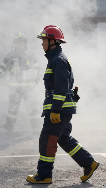 Side view of an East Asian firefighter in turnout gear walking through thick hazy smoke