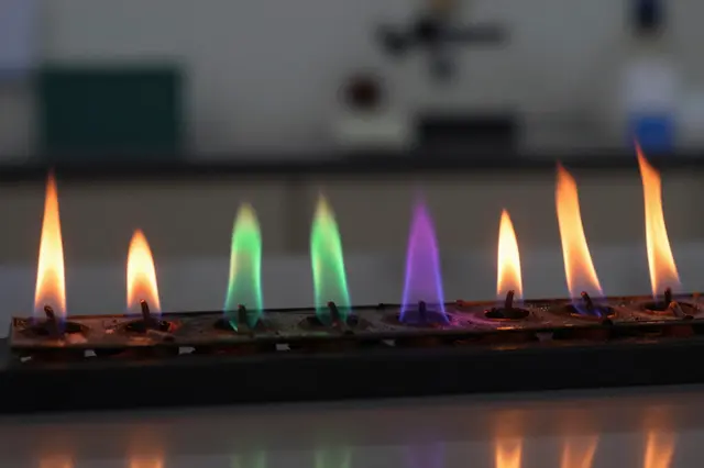 Row of multicolored flames from a laboratory burner set against a blurred dark lab background