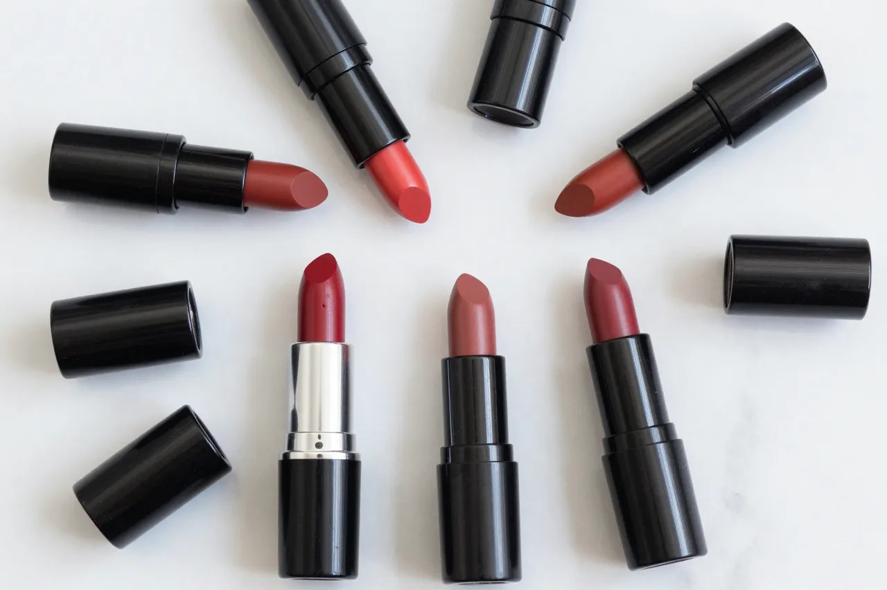 Unlabeled lipsticks in red, coral and berry tones with removed caps arranged on a smooth white marble surface