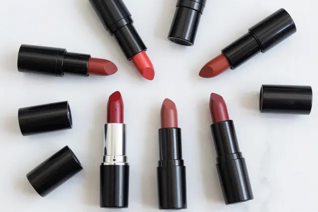Unlabeled lipsticks in red, coral and berry tones with removed caps arranged on a smooth white marble surface