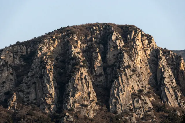 Sheer rocky cliffs of a flat topped mountain glow in soft early morning light under a pale clear sky