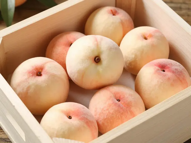 Ripe white peaches rest in a paper-lined light wooden crate on a wooden surface