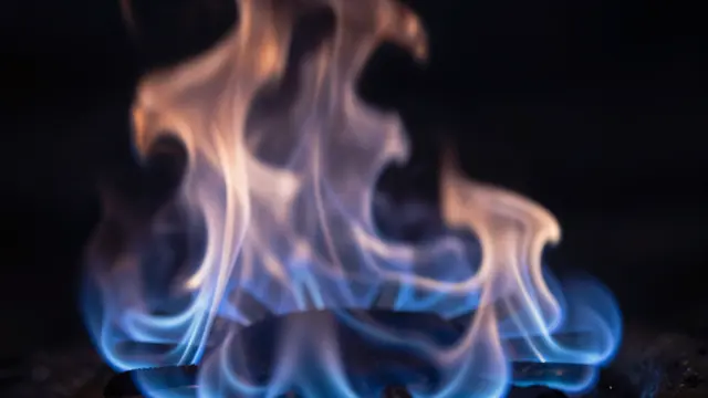 Wispy blue and warm orange flames rise against a solid dark black background