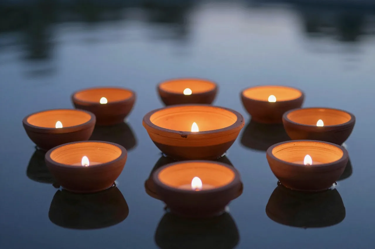 Lit terracotta diya lamps float on calm still water during twilight hours