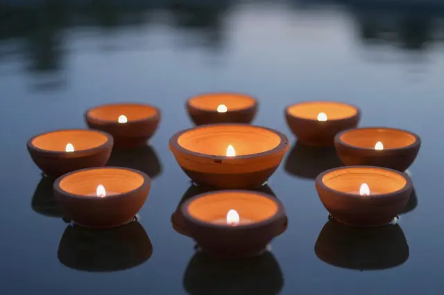 Lit terracotta diya lamps float on calm still water during twilight hours
