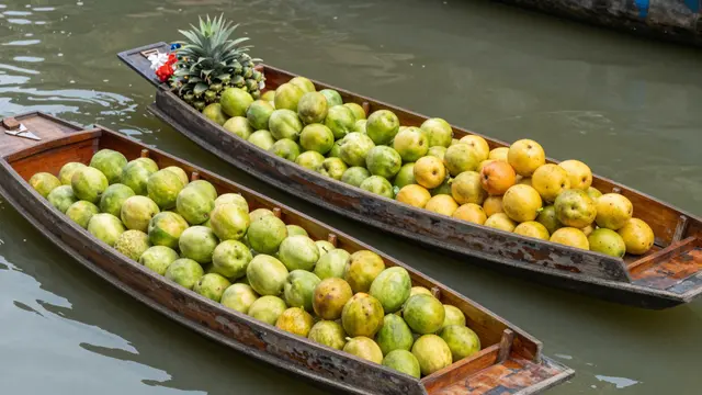 Two weathered wooden market boats loaded with fresh fruit sit on calm canal water
