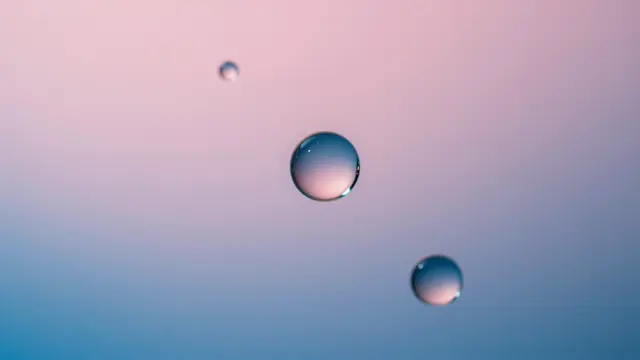 Three oil droplets acting as tiny lenses over a smooth pink to blue gradient background