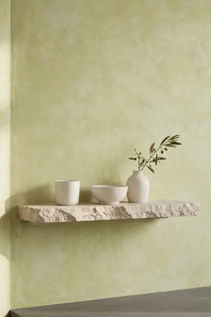 A rough floating stone shelf holds plain white ceramics against a soft limewashed plaster wall.