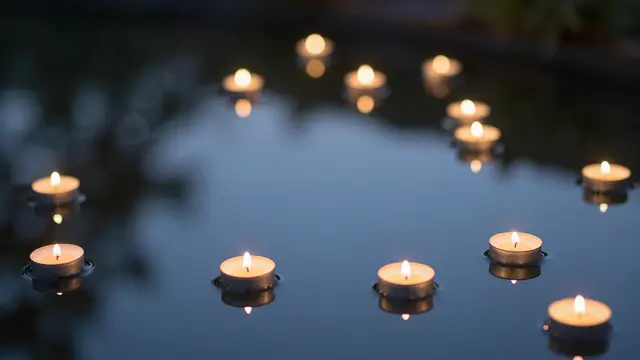 Lit tealight candles float on still dusk pond water with soft glowing reflections