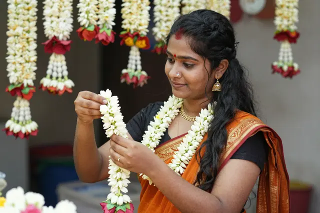 South Asian female florist threads jasmine flowers into a garland at her flower stall