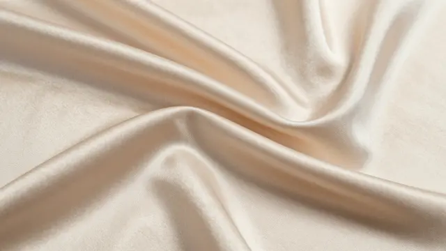 Close-up of soft champagne satin fabric with natural flowing folds and subtle sheen