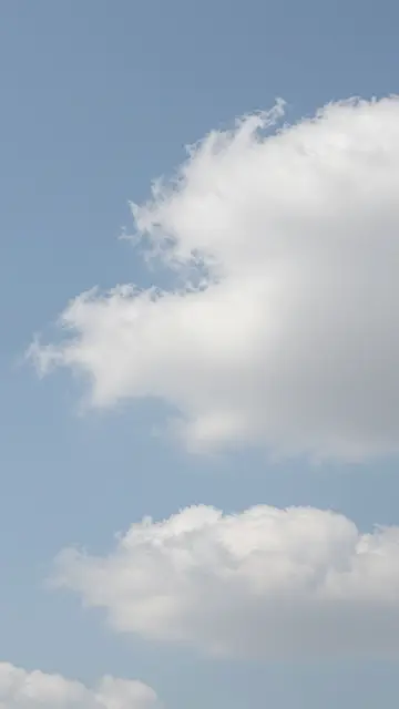 Looking up at soft fluffy white clouds drifting across a pale light blue sky