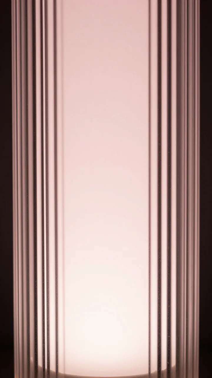 Full frame close-up of vertical fluted glass with soft pale pink backlighting