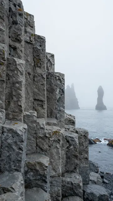 Columnar basalt cliff overlooks fog shrouded sea stacks on a misty coast