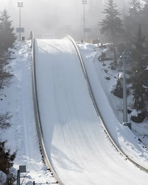 Looking up at an empty snow-covered ski jump ramp shrouded in soft winter fog
