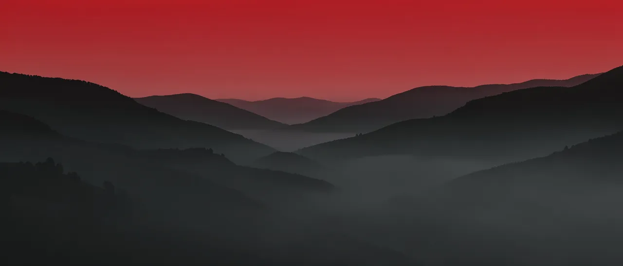 Layered charcoal hills fade into soft fog beneath a gradient deep red sky