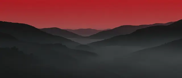 Layered charcoal hills fade into soft fog beneath a gradient deep red sky
