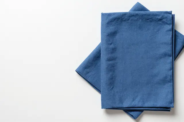 Top view of stacked folded blue linen cloth in the lower right of a plain white table with empty copy space