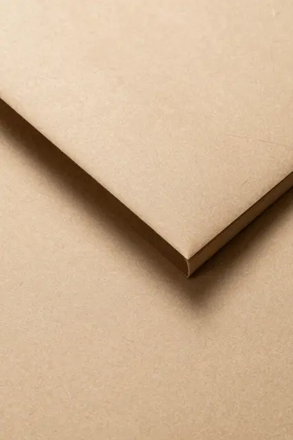 Top view close-up of light brown kraft paper with a single soft folded corner over a matching kraft paper surface