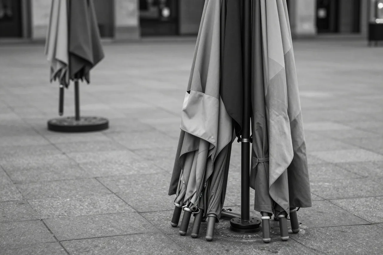 Folded patio market umbrellas stand in an empty paved public square in black and white