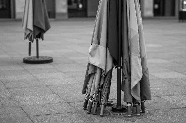 Folded patio market umbrellas stand in an empty paved public square in black and white