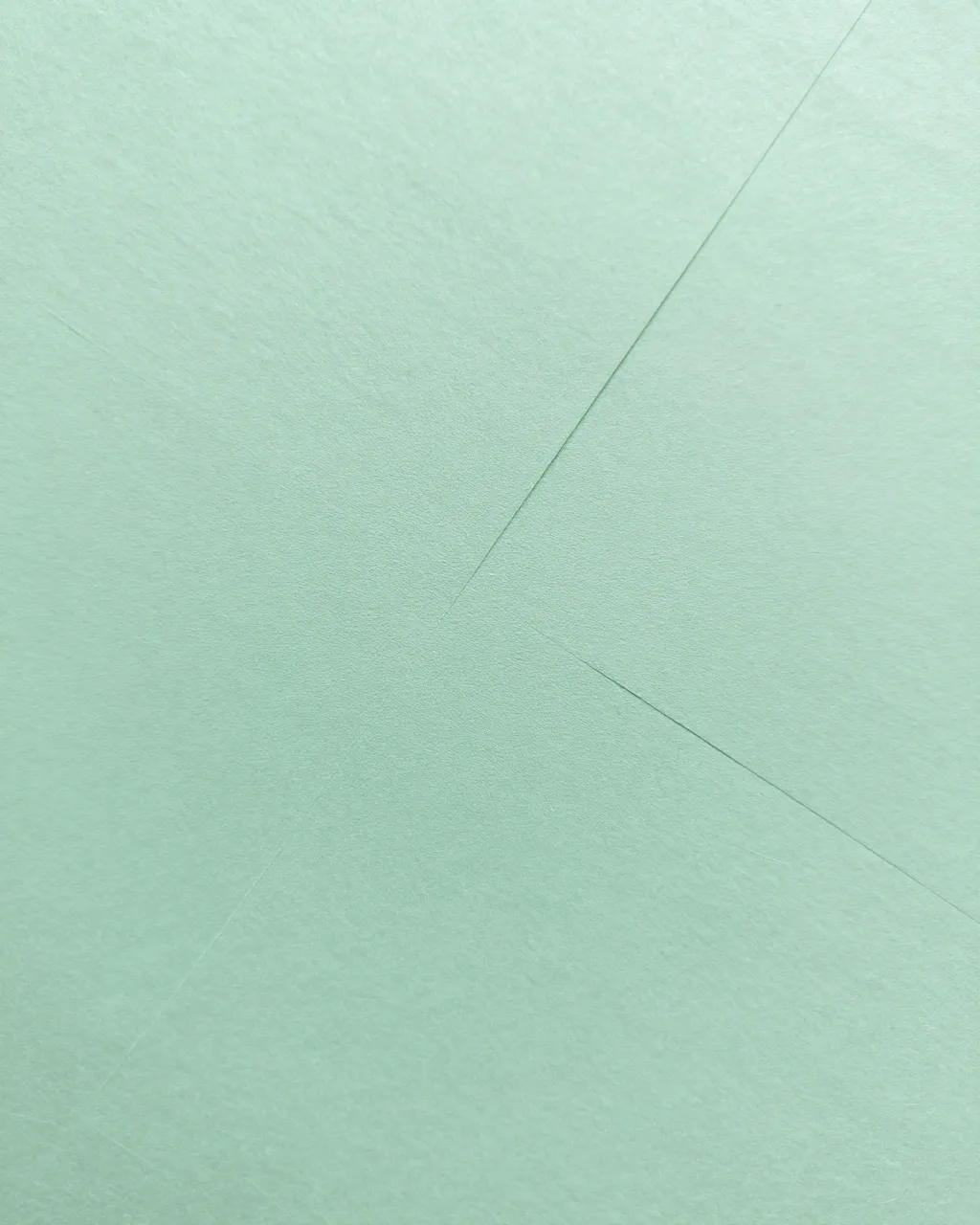 Full frame close-up of light mint green paper with crisp diagonal fold lines under even flat lighting