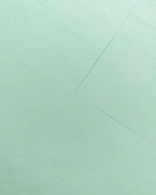 Full frame close-up of light mint green paper with crisp diagonal fold lines under even flat lighting