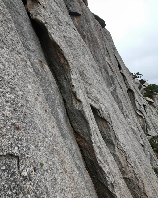 Tilted view of a mountain cliff with tightly folded layered granite rock under overcast sky