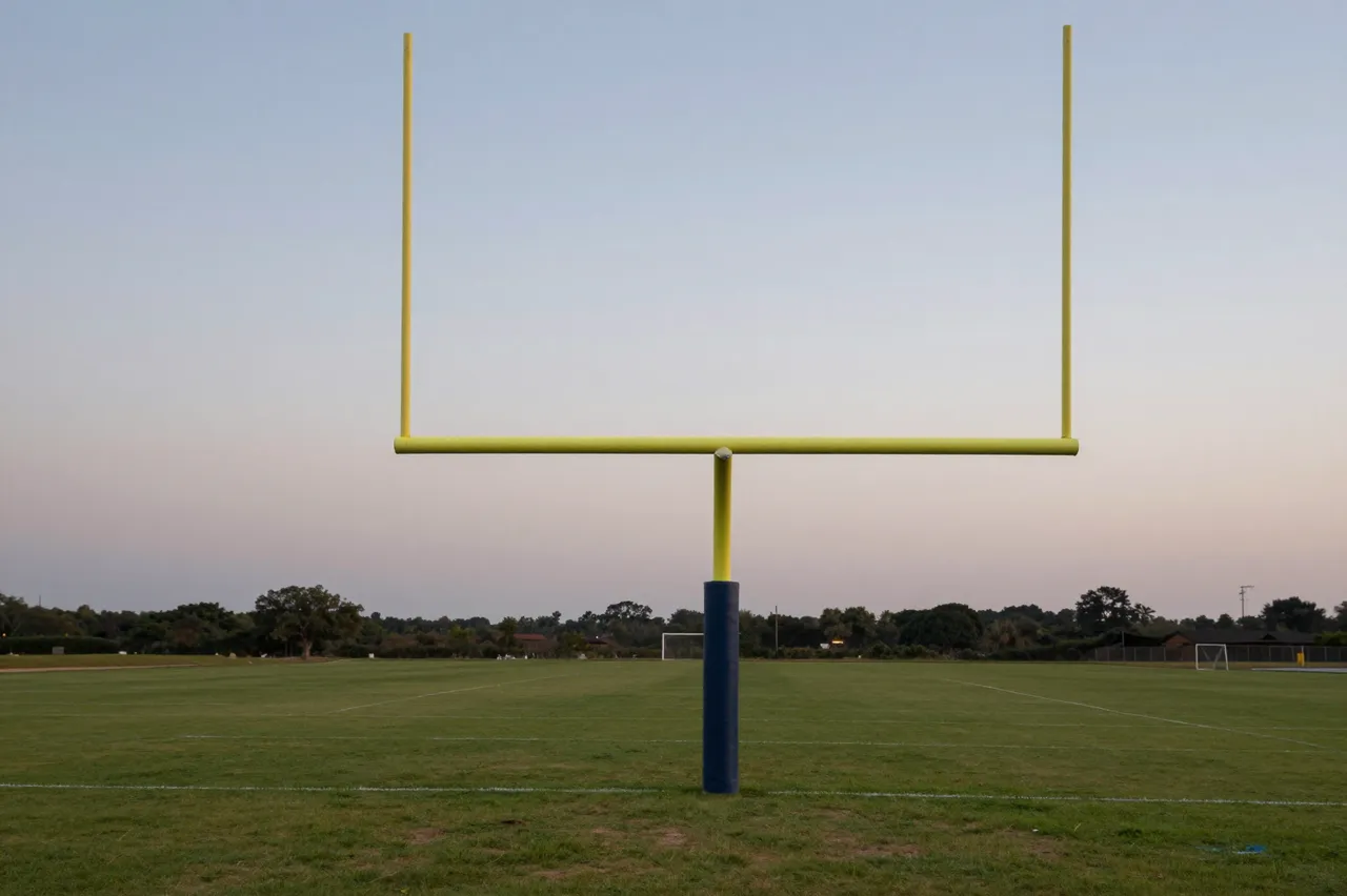 Yellow American football goal post stands on an empty grass field under a pale dusk sky