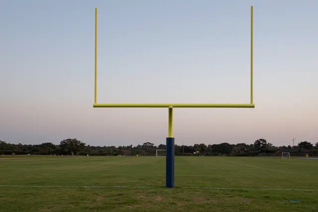 Yellow American football goal post stands on an empty grass field under a pale dusk sky