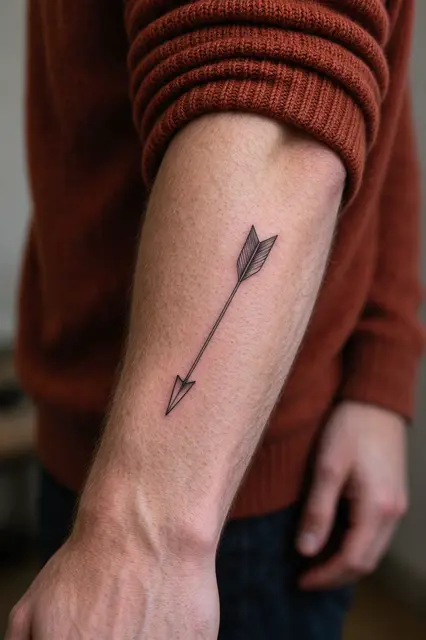 Close-up of a fine line arrow tattoo on a forearm with a rolled rust knit sweater sleeve