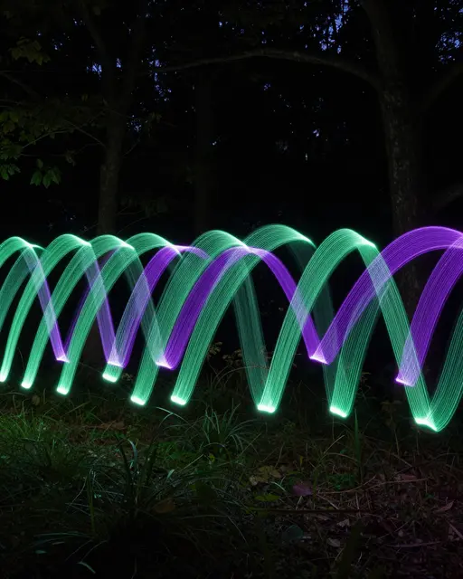 Glowing wavy green and violet light trails arc across a dark nighttime forest clearing