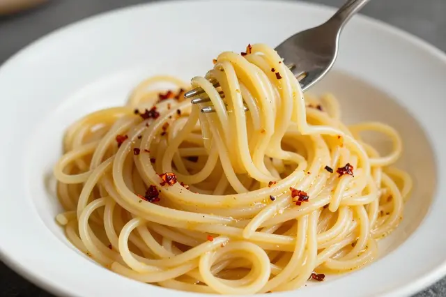 A metal fork twirls seasoned spaghetti with chili flakes in a white ceramic bowl