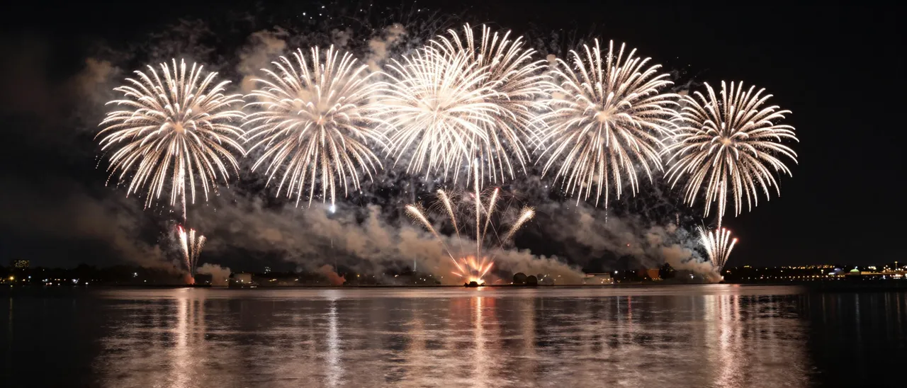 Panoramic golden fireworks burst over calm night water with glowing mirrored reflections