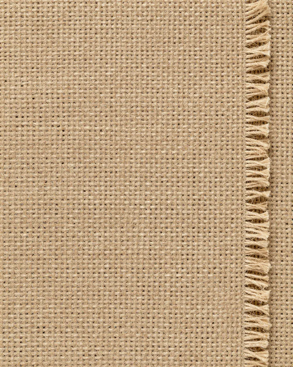 Close-up view of natural woven burlap fabric with a frayed fringed edge along the right side