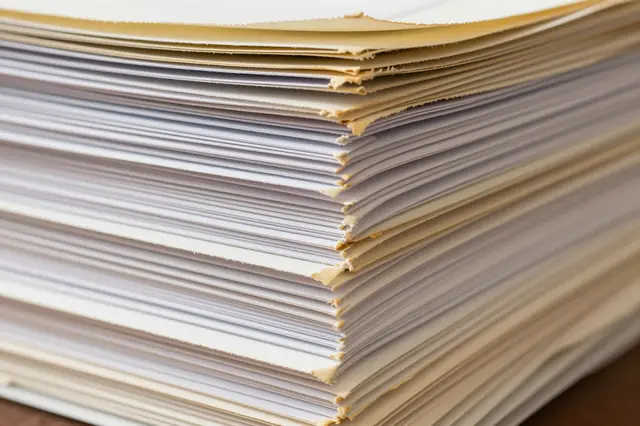 Close-up side view of a tall stack of old paper sheets with worn yellowed frayed edges