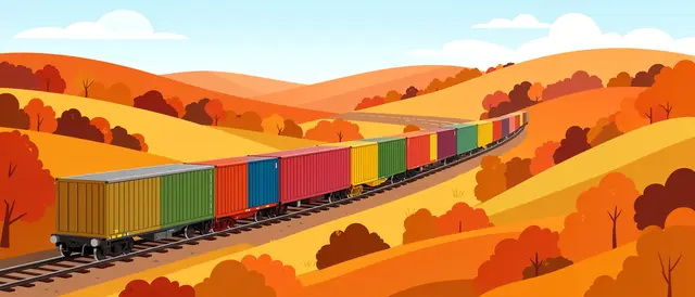 A long colorful boxcar freight train travels along tracks winding through rolling autumn hills under a pale blue sky