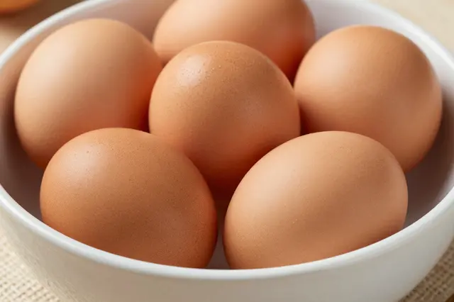 Several fresh brown farm eggs resting inside a white ceramic bowl on a woven surface