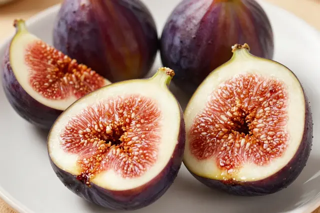 Whole and halved ripe purple figs arranged neatly on a plain white ceramic plate.