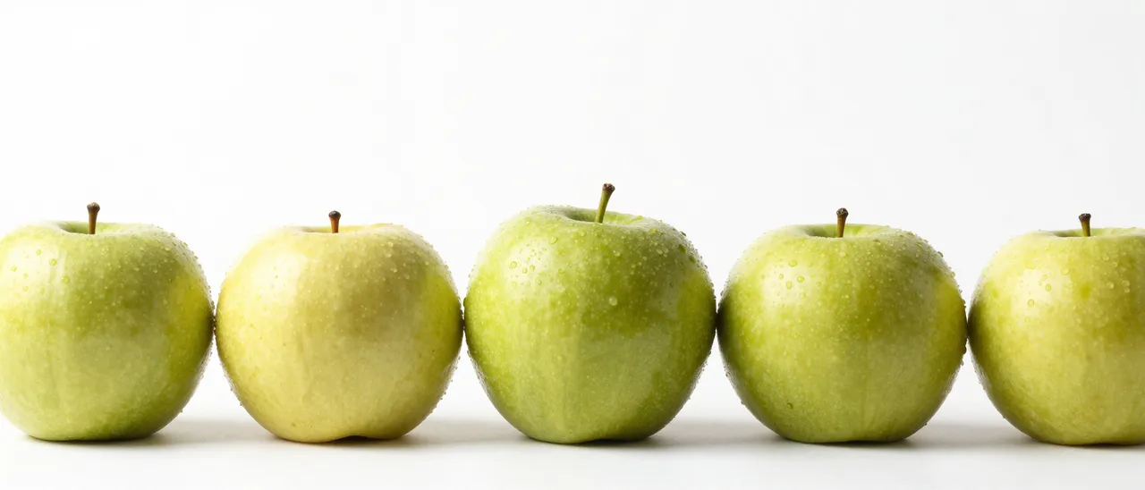 Five dewy green apples arranged in a straight row along the bottom of a plain white background with empty copy space above.