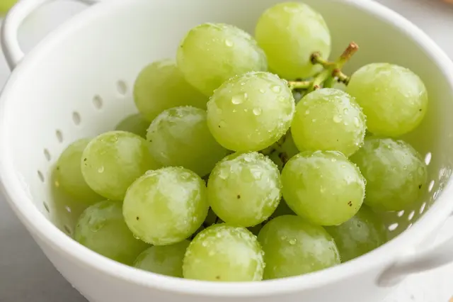 Washed green grapes with water droplets sit inside a white perforated colander