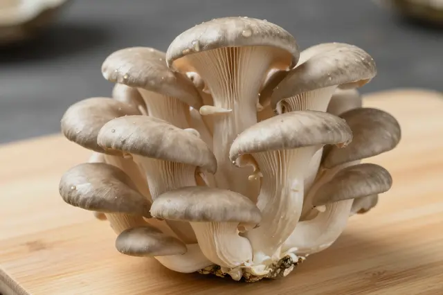 A tight cluster of fresh oyster mushrooms rests on a light wooden cutting board