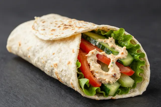 Stuffed flatbread wrap with crisp vegetables and creamy sauce resting on a dark slate surface
