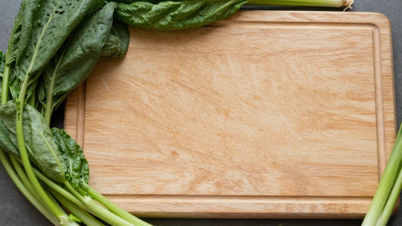 Top-down view of an empty wooden cutting board framed by leafy green vegetables on a dark countertop.