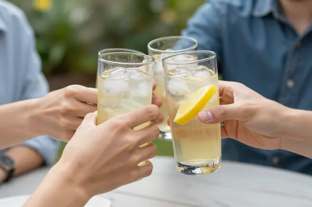 Partial view of people clinking tall glasses of iced lemonade over an outdoor garden table