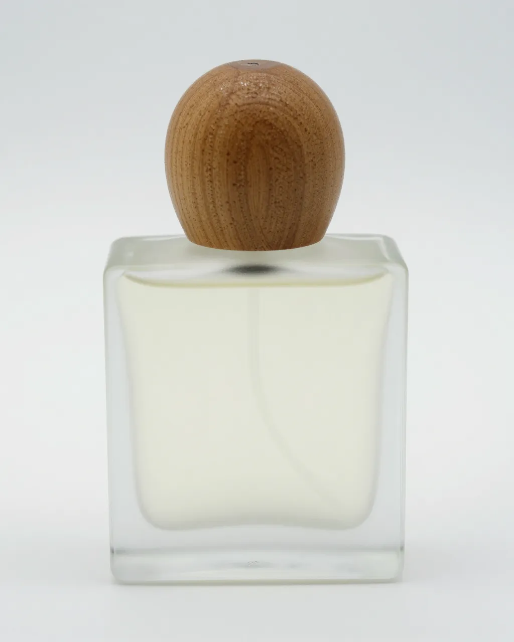 Square frosted glass perfume bottle with round wooden cap on a plain light studio background
