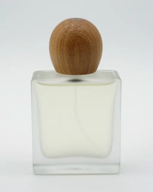 Square frosted glass perfume bottle with round wooden cap on a plain light studio background