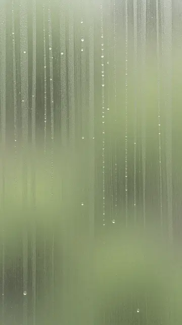 Vertical sandblasted glass with trailing water droplets against soft muted green light